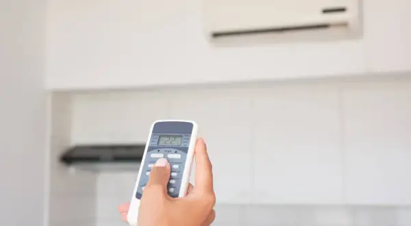 Mano che regola il telecomando del condizionatore in modalità "DRY" per un clima più asciutto.