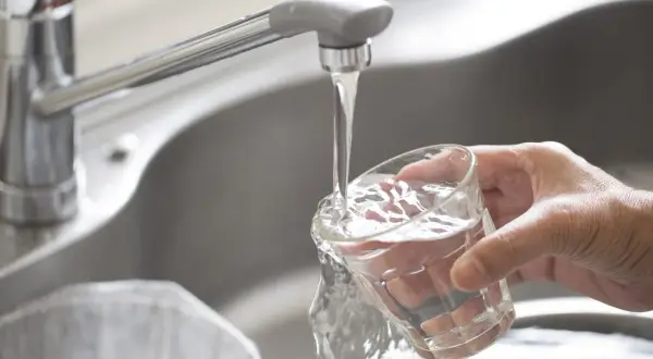 Main d'une personne remplissant un verre d'eau du robinet à Paris. L'eau claire coule du robinet chromé dans le verre.