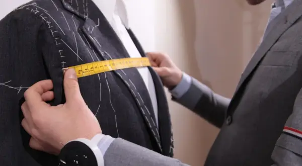 Sarto misura la giacca con metro giallo, prendendo nota della lunghezza braccio uomo per una vestibilità perfetta.
