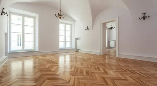 Un ampio salone con parquet a spina di pesce appena levigato, illuminato da grandi finestre e lampadari antichi.