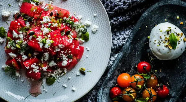 Salade de pastèque, feta, pistaches et tomates cerises, avec une burrata crémeuse. Un délice estival qui rappelle la tomate mozzarella.