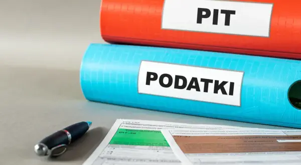 Dwa segregatory z napisami "PIT" i "PODATKI", obok formularze podatkowe i długopis. Kto nie płaci podatku do 26 roku życia?