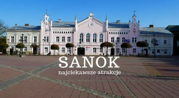 Różowy budynek ratusza na rynku w Sanoku, z napisem "Sanok najciekawsze atrakcje".