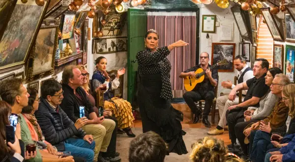 Artistas flamencos de Granada actúan en un tablao íntimo, con una bailaora en primer plano y un guitarrista acompañando.