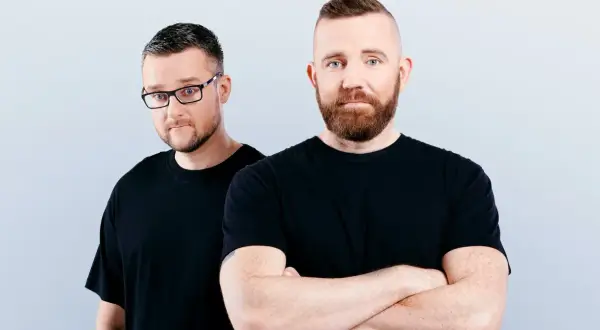 Dwóch mężczyzn w czarnych koszulkach, jeden w okularach, drugi ze skrzyżowanymi rękami. Wyglądają jak duet Catz n Dogz.