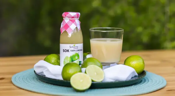 Butelka soku z limonki i szklanka orzeźwiającego napoju, otoczone świeżymi owocami. Odkryj sok z limonki właściwości!