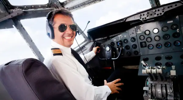 Uśmiechnięty pilot w okularach przeciwsłonecznych i słuchawkach w kokpicie. Zastanawiasz się, ile zarabia pilot samolotu?