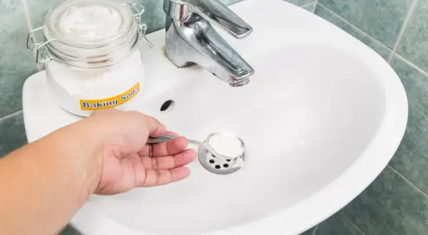 Une main verse du bicarbonate de soude dans un évier, une méthode naturelle pour le déboucheur canalisation maison.
