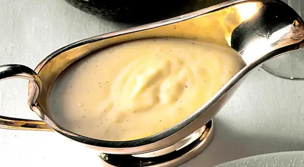 Krämig vaniljsås med små prickar av vaniljsocker i en elegant silverkanna, redo att serveras.