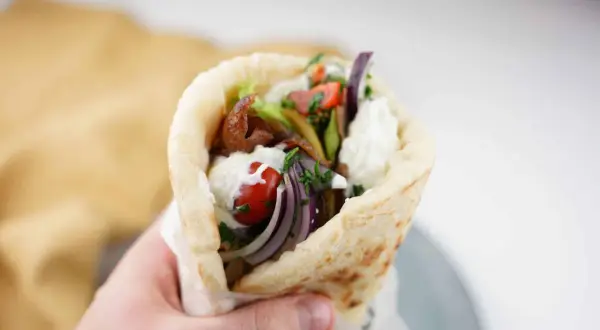 En hand håller en gyros med kött, grönsaker och sås. Perfekt för en supergod fredagsmat!