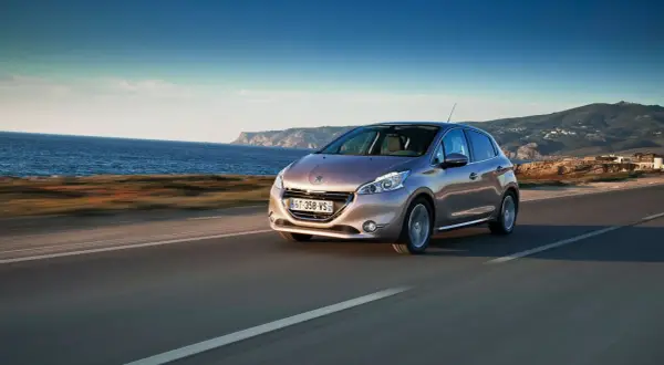 En Peugeot 208 kör längs en kustväg med havet till vänster och berg i bakgrunden. En perfekt bild för ett peugeot 208 test.