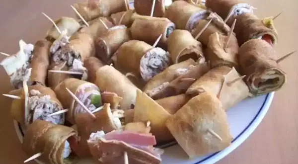 Assiette de crêpes roulées garnies, parfaites pour un apéro convivial. Des bouchées savoureuses prêtes à être dégustées.
