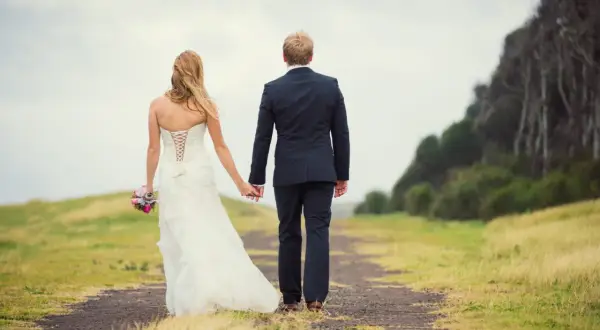 Un couple de jeunes mariés se promène main dans la main sur un chemin, un bouquet à la main. Un beau mariage au mois de mai.