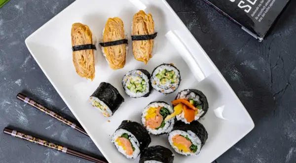 Pyszne domowe sushi przepis na talerzu: nigiri z omletem tamago, rolki z łososiem i warzywami, ogórkiem i sezamem.