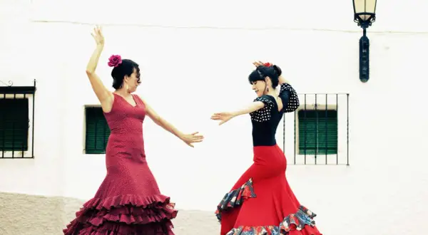 Dos mujeres bailan flamenco, con faldas rojas y volantes. Una lección de baile flamenco para principiantes.