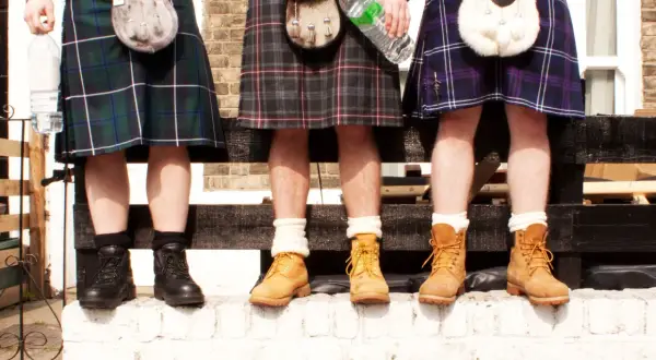 Trzech mężczyzn w kiltach, z torbami na pasie. Czy pod kiltem nosi się bieliznę? Ich nogi są odsłonięte, co sugeruje tradycję.