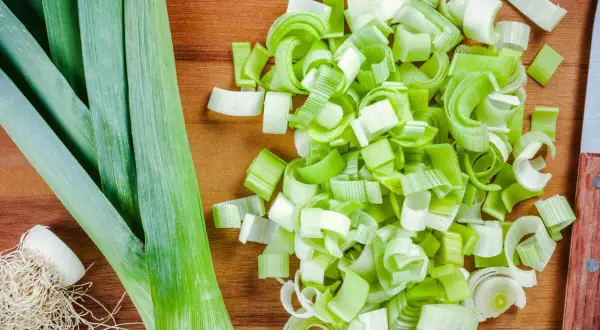 Frischer Lauch, bereit für leckere porree rezepte. Ganze Stangen und fein geschnittene Ringe liegen auf einem Holzbrett.