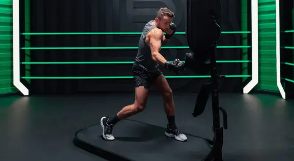 An orthodox fighter trains intensely, throwing punches at a boxing dummy in a modern gym with neon green accents.