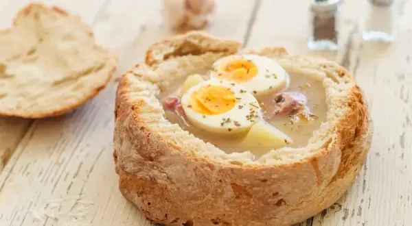Gotowy zakwas na żurek w chlebie, z jajkiem i ziemniakami. Obok kromka chleba i przyprawniki.