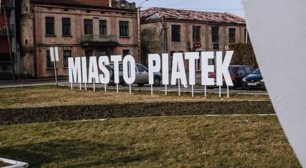 Napis "Miasto Piątek" na tle starych kamienic. To środek Polski, gdzie każdy dzień może być jak piątek.