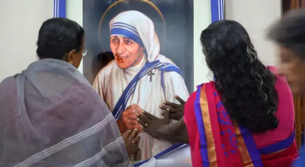 Frauen berühren ein Bild von Mutter Teresa, die ihr Leben den Armen widmete.