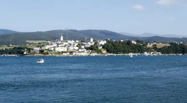 Vista del mirador de Ribadeo con casas blancas y el mar azul. Un pequeño barco navega en la distancia.
