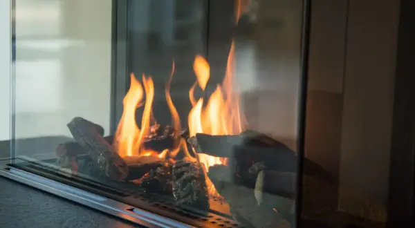 Flammen tanzen um Holzscheite in einem modernen Kamin. Ein Blick, der zeigt, wie man Ascheflecken entfernen kann, ohne die Gemütlichkeit zu stören.