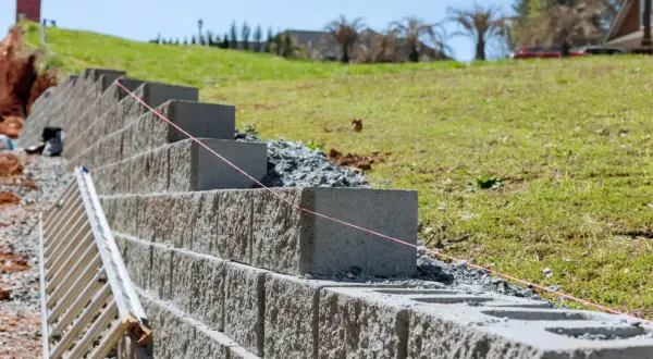 Budowa muru oporowego z betonowych bloków, z drabiną i czerwoną nicią do poziomowania.