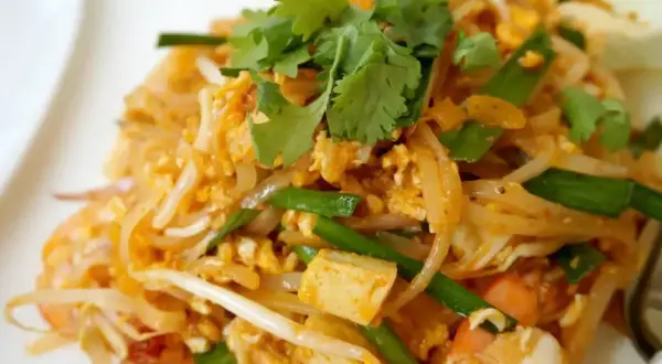 Pyszne makaron po tajsku z krewetkami, tofu, jajkiem i szczypiorkiem, udekorowany świeżą kolendrą.