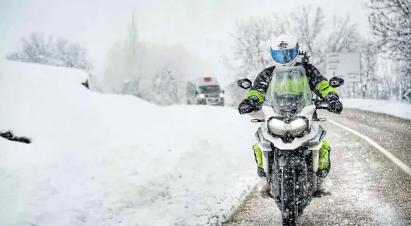 Motocyklista w kasku i zimowej odzieży jedzie po zaśnieżonej drodze.
