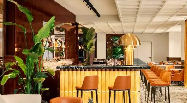 Interni eleganti del Bulgari Hotel Roma: bancone bar dorato, sedie in pelle arancione, piante lussureggianti e un'atmosfera sofisticata.
