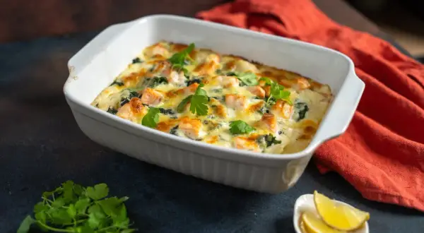 Herzhafte Lachs Spinat Lasagne, goldbraun überbacken, garniert mit frischer Petersilie. Dazu Zitronenspalten.