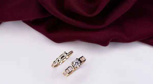 Dos anillos de oro, uno de compromiso con diamante y otro de alianza con diamantes pequeños, listos para combinar.