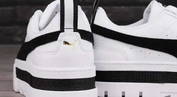 Białe buty sportowe Puma Mayze Leather z czarnymi akcentami i złotym logo. Gruba podeszwa dodaje im charakteru.