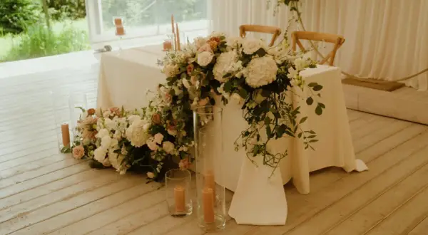 Elegancki stół prezydialny ozdobiony bujną wiązanką kwiatów i świecami.