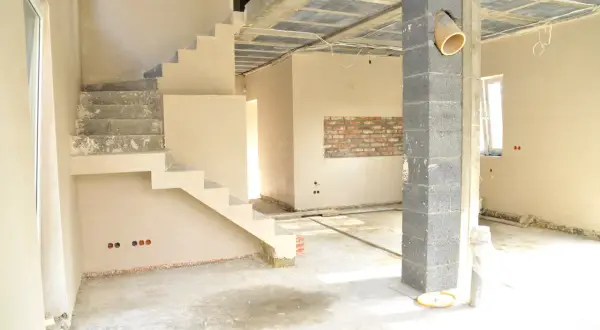 Wnętrze w trakcie budowy, schody i ściany pokryte tynkiem cienkowarstwowym wewnętrznym. Betonowy słup i sufit z widocznymi instalacjami.