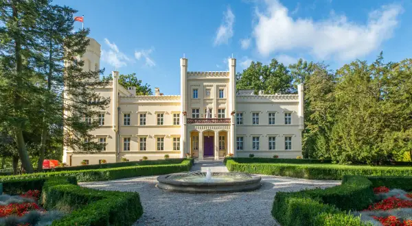 Jasny pałac z wieżą, jeden z pięknych zamków w lubuskim, otoczony ogrodem z fontanną i kwitnącymi rabatami.