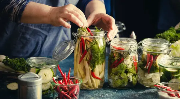 Ręce układają warzywa i papryczki chili do słoików, przygotowując je do tego, jak zawekowac sloiki.