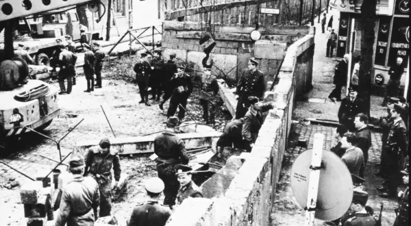 Militär och civila vid Berlinmuren, en scen som kan illustrera kalla kriget tidslinje. En kran lyfter bort delar av muren.