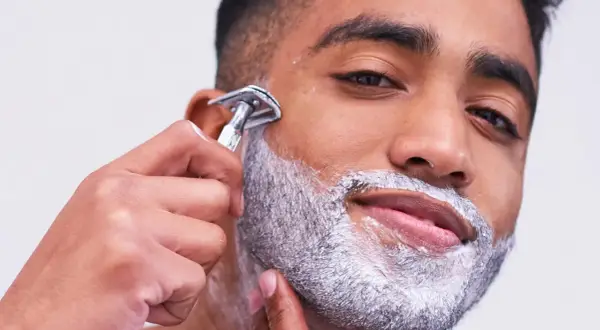 Uomo con schiuma da barba aggrappante prima della rasatura, mentre usa un rasoio di sicurezza.