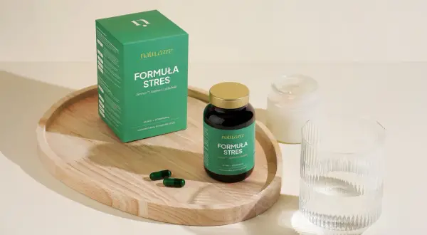Zielone opakowanie i kapsułki suplementu diety "Formuła Stres" na drewnianej tacy, obok szklanki wody i świecy.