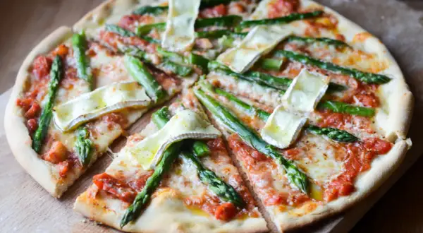 Pyszna pizza ze szparagami i serem brie, polana sosem pomidorowym, pokrojona na kawałki.