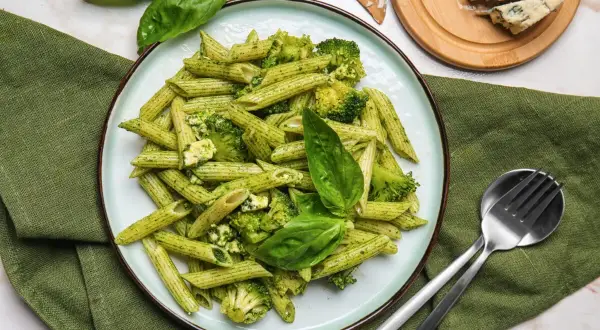 Penne z brokułami i serem gorgonzola w sosie pesto, udekorowane listkami bazylii. Idealne danie dla miłośników makaronu.