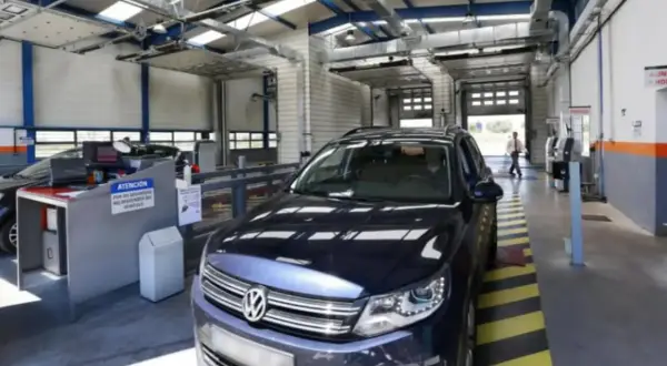 Un coche oscuro en un centro de inspección técnica, listo para pasar la ITV. El personal revisa los papeles.