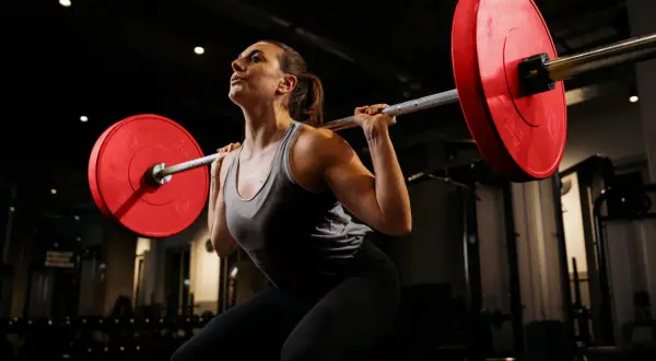 Frau mit Langhantel im Fitnessstudio, konzentriert auf Kniebeugen für Muskelaufbau.