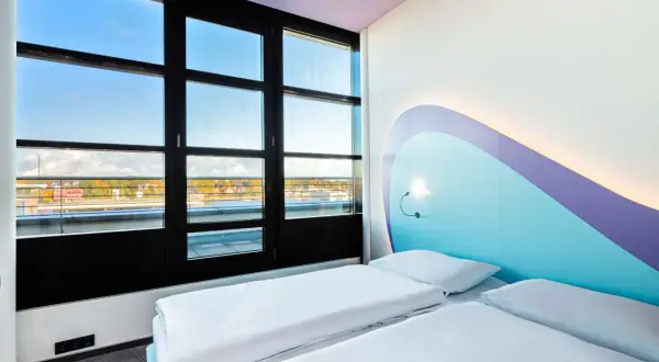 Pokój z dwoma łóżkami w **Radisson Blu Hotel Rostock**. Duże okno z widokiem na miasto i wodę. Nowoczesne, jasne wnętrze z kolorowym zagłówkiem.