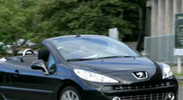 Czarny kabriolet Peugeot 207 CC z opuszczonym dachem jedzie po drodze.
