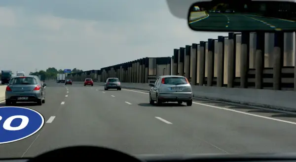 Panneau de signalisation au sol indiquant la vitesse minimale autoroute de 80 km/h. Plusieurs voitures circulent sur la voie rapide.