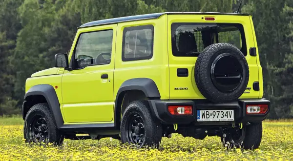 Jaskrawożółty Suzuki Jimny na tle łąki z żółtymi kwiatami. Sprawdź aktualną suzuki jimny cena i możliwości tego terenowego auta.
