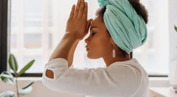Mujer con turbante turquesa y pendientes largos medita. A veces, cuando me enfado y no respiro, busco la calma así.